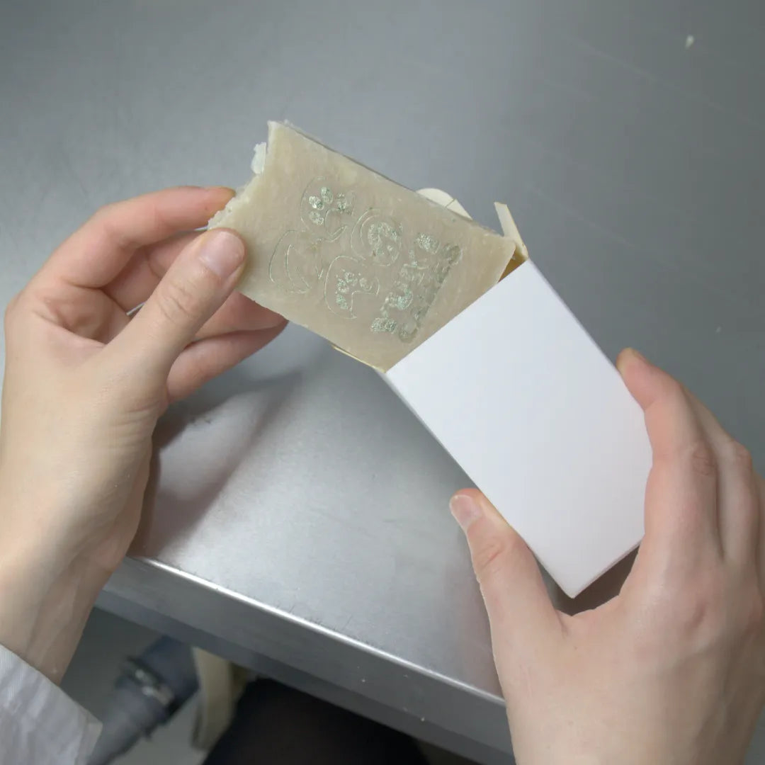 Zwei Hände stecken ein mit Yuki cares Logo geprägtes Stück Maukeseife in eine weiße Box auf einem Tisch.