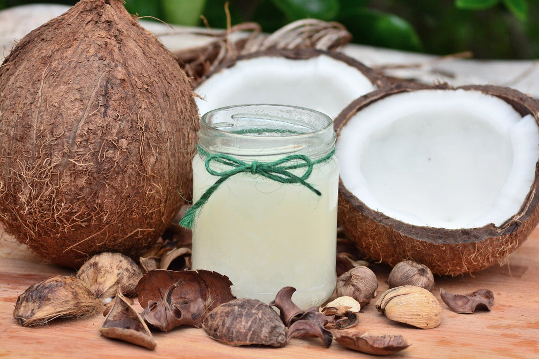 Kokosöl im Glas neben Kokosnüssen