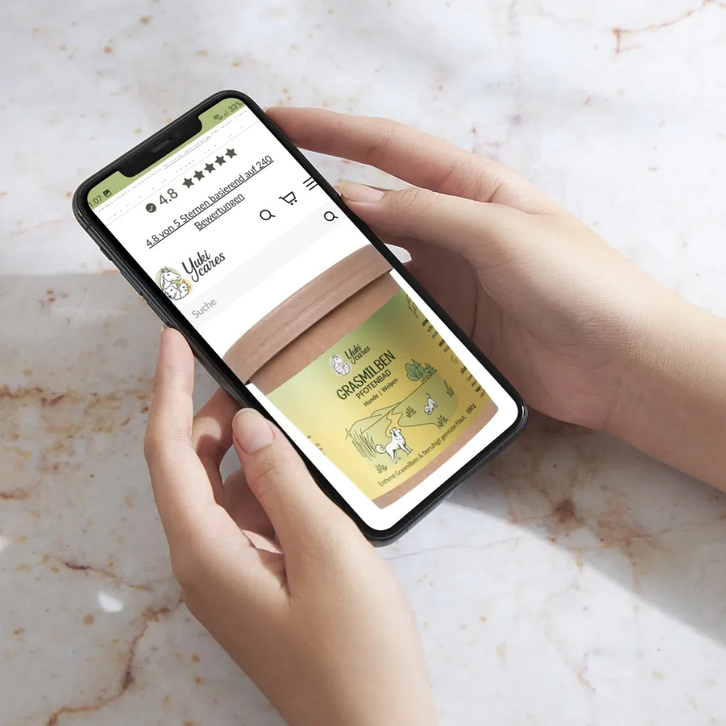 Eine Person hält ein Smartphone, das eine Webseite mit einem Produkt gegen Grasmilben anzeigt.