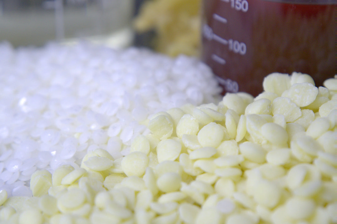 Nahaufnahme von weißen Montanov- und gelben Kakaobutterpastillen neben einem Messbecher auf einem Tisch.