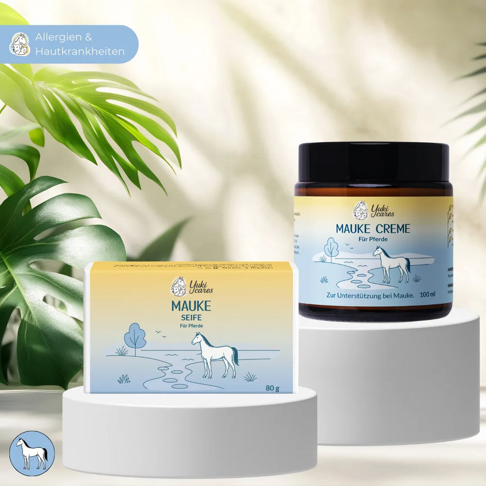Zwei Produkte für Pferdepflege, Mauke Seife und Creme, stehen auf Podesten, umgeben von grünen Blättern.