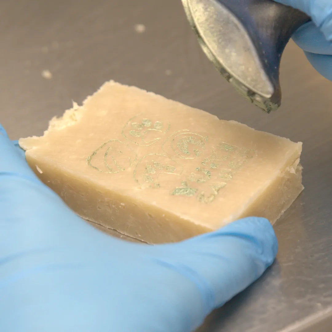 Eine Person mit blauen Handschuhen prägt mit einem Stempel das Yuki cares Logo in ein Stück Seife.