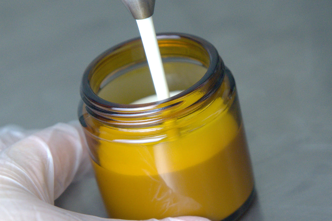 Eine Person gießt eine weiße Flüssigkeit in ein braunes Glas, während sie Handschuhe trägt.