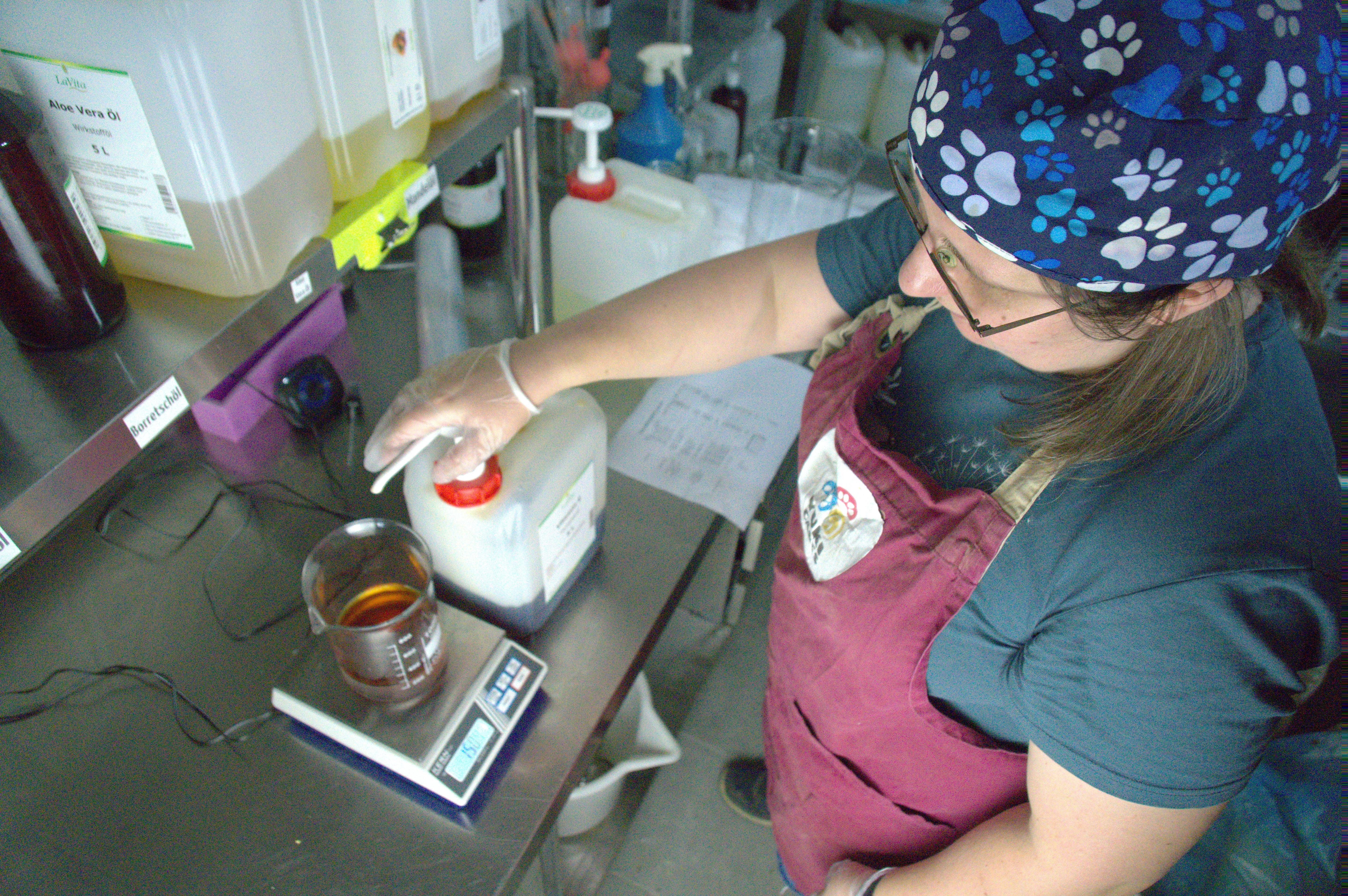 Eine Frau in Schürze wiegt Flüssigkeit in einem Messbecher auf einer digitalen Waage ab.