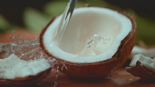 Eine aufgeschlagene Kokosnuss auf die in Zeitlupe Wasser gekippt wird
